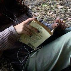 a woman sitting on the ground reading a book with earphones attached to her ears