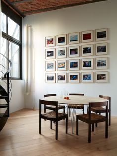 a dining room table with four chairs and pictures on the wall above it in front of a spiral staircase