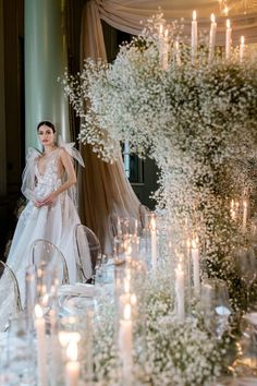 a woman standing in front of a table filled with white flowers and candles