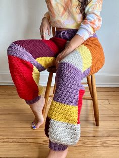 a woman is sitting on a chair wearing colorful crocheted leggings and smiling