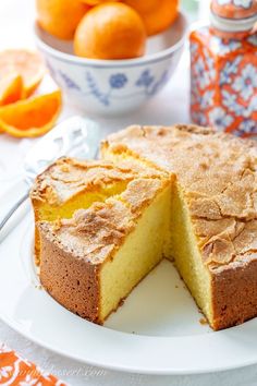 a cake on a plate with one slice cut out and oranges in the background