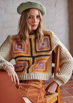 a woman sitting in a chair wearing a crocheted sweater and hat with her hands on her hips