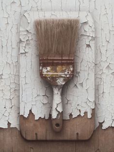 a paint brush is hanging on the side of a white painted wooden wall with peeling paint