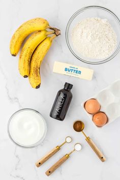 ingredients to make banana bread laid out on a white marble counter with bananas, eggs and flour