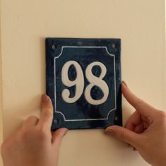 two hands are holding up a blue and white plaque with the number 98