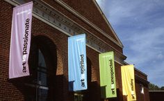 colorful banners hanging from the side of a brick building on a sunny day with blue skies in the background