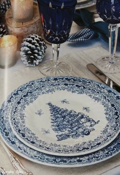 the table is set with blue and white plates, silverware, and pine cones