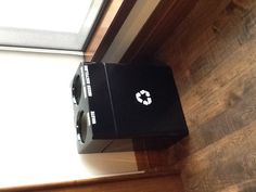 a black trash can sitting in front of a window next to a wooden floor and wall