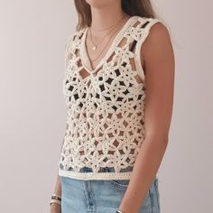 a woman wearing a white crochet top and denim shorts with her hands in her pockets