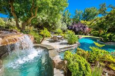 an outdoor swimming pool surrounded by greenery and water features is pictured in this image