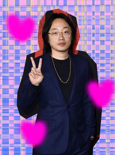 a man in a blue suit and red hoodie making the peace sign with his hand