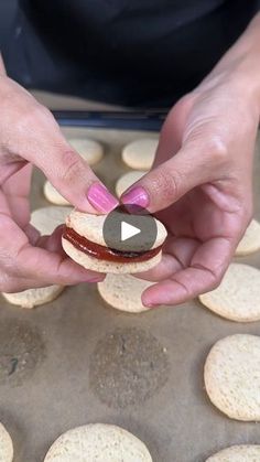 two hands are holding small crackers in the shape of hamburgers on a baking sheet