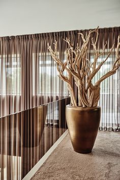 a vase with some branches in it sitting on the floor next to a curtained window