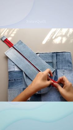 someone is sewing on some blue jeans with a red tape and scissors in their hands