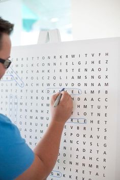 a man writing on a large white board with letters and numbers in front of him