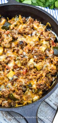 a skillet filled with meat and vegetables on top of a wooden table next to parsley