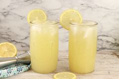 two glasses filled with lemonade sitting on top of a counter next to a shaker