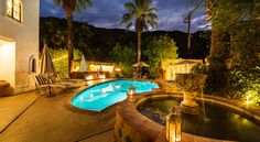 an outdoor swimming pool surrounded by palm trees at night with lights on and chairs around it