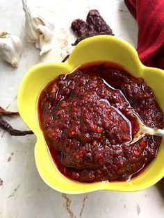 a yellow bowl filled with chili sauce on top of a counter next to some garlic