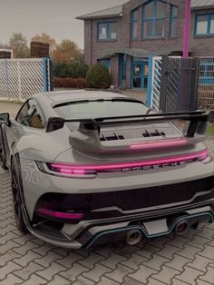 a grey sports car parked in front of a house with pink lights on the hood