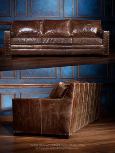 two leather couches sitting next to each other in front of a blue wall and wooden floor