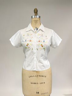 "Another utterly adorable vintage blouse from the 1950s! Soft, lightweight cotton or cotton blend with button front, small collar and short sleeves. Front of blouse is embroidered with little people in sombreros, cactus, palm trees and women in full skirts. No labels present, was likely purchased as a souvenir from a vacation taken long ago. Very good condition, faint dark line from shoulder halfway down (that looks to be a manufacturing defect from the cotton) and not really a flaw. Small white Retro White Cotton Blouse, Vintage White Summer Blouse, Vintage White Blouse For Summer, White Cotton Retro Blouse, Vintage Embroidered Summer Shirt, Retro Embroidered Cotton Shirt, Retro Embroidered Collared Top, Vintage Embroidered Button-up Shirt, Retro Embroidered Summer Shirt