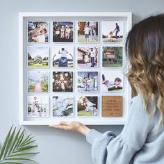 a woman holding up a white framed photo with photos on the wall in front of her