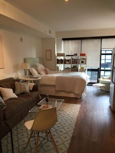 a living room filled with furniture and a large window next to a bed on top of a hard wood floor