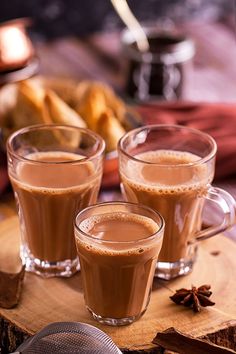 three glasses of hot chocolate drink on a wooden board with cinnamons and apples in the background