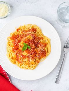 a plate of spaghetti with sauce and parmesan cheese on the side next to silverware