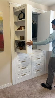 a man standing in front of a white cabinet with drawers and shelves on the wall