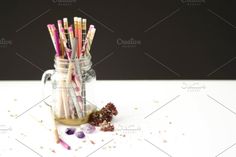 a jar filled with lots of different colored pencils next to some dried flowers on a white table