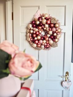 a christmas wreath hanging on the front door next to a vase with flowers in it