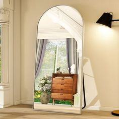 an arched mirror in the corner of a room with a dresser and lamp on it