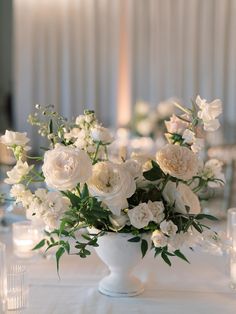 a vase filled with white flowers sitting on top of a table next to some candles