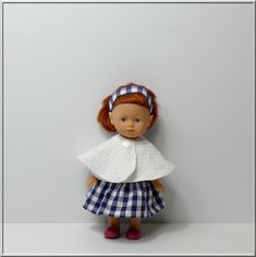 a doll with red hair wearing a blue and white checkered dress standing against a gray wall