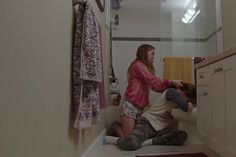 two people are sitting on the floor in a bathroom and one person is holding onto the toilet