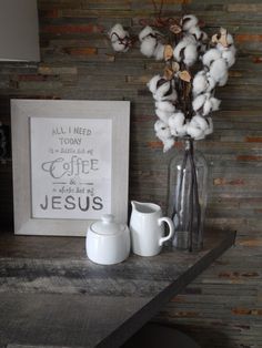 cotton in a vase and two mugs on a wooden table next to a sign