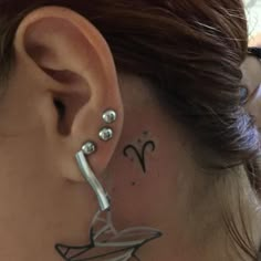 a woman's behind the ear has a small tattoo on her left ear and is wearing a pair of silver hoop earrings