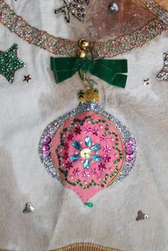 a pink ornament hanging from a green ribbon on a white shirt with sequins