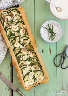 a table topped with a long loaf of bread covered in cucumbers and cheese