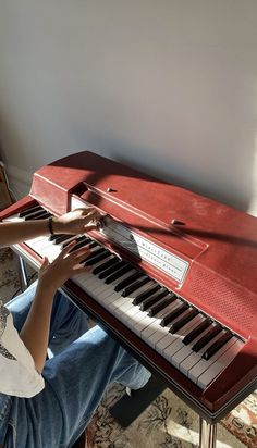 a person sitting at a red piano with their hands on the keys and playing it