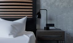 a bed with white sheets and pillows next to a wall mounted lamp in a bedroom