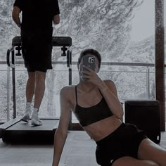 a woman is taking a selfie in front of a man on a treadmill