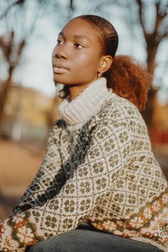 a woman sitting on top of a wooden bench wearing a sweater and black pants, looking off into the distance