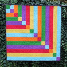 a multicolored quilt hanging from a black metal bar on a green wall covered in ivy