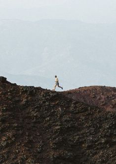 a person running on top of a rocky hill with mountains in the backgroud