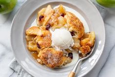 an apple cobbler on a plate with ice cream and two green apples in the background