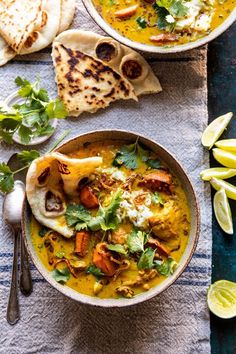 two bowls filled with soup next to pita bread and lime wedges on the side