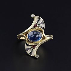 A striking Egyptian Revival ring (circa 1910) with black white and red enamel and a natural blue sapphire at its center.  Two tiny diamonds add a glittery flourish on each point of the ring.  The sapphire cabochon is moderate blue in color and weighs approximately 2.16ct.   The face of the 18k gold ring measures 1 inch tall by 0.4 inches wide, and it is in great condition.  The ring is a size 6.75, but it can be resized free of charge.  It weighs 6.14 grams.  We have many other fantastic offerin Art Deco Diamond Cabochon Rings, Art Deco Enamel Rings For Formal Occasions, Art Deco Diamond Rings With Cabochon, Art Deco Yellow Gold Enamel Ring For Formal Occasions, Formal Enamel Ring With Gemstone, Gold Art Deco Enamel Ring, Art Deco Formal Yellow Gold Enamel Ring, Formal Yellow Gold Art Deco Enamel Ring, Formal Art Deco Yellow Gold Enamel Ring